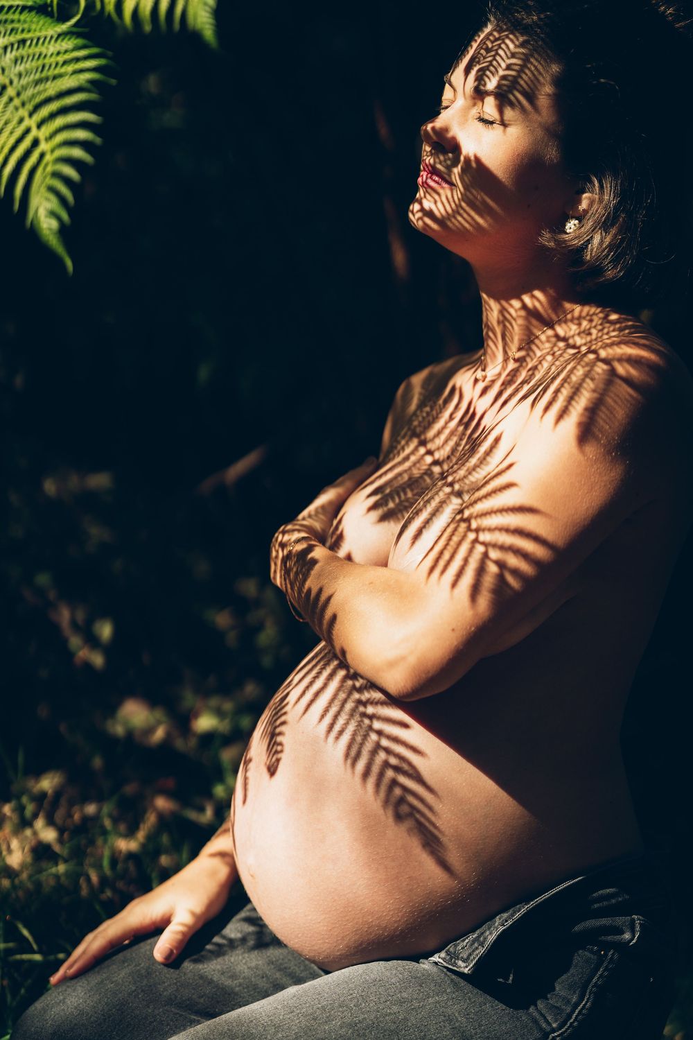 Beautiful maternity photo with fern leaf shadows creating patterns across a pregnant belly in warm natural sunlight.