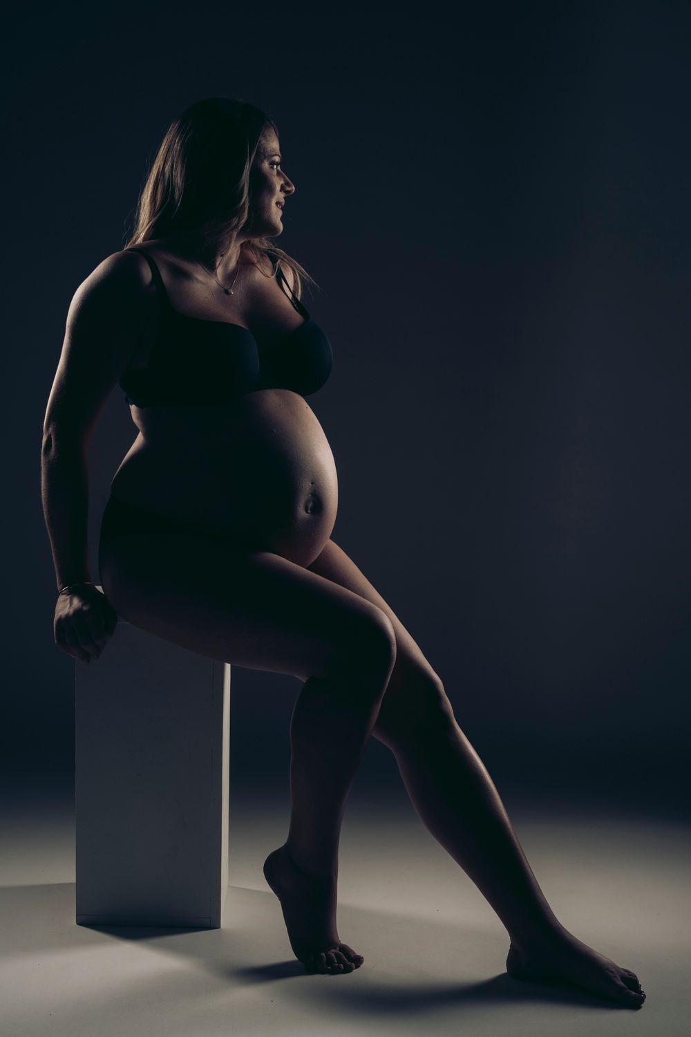 Silhouetted figure in dramatic lighting poses artistically with a geometric cube shape against dark background.