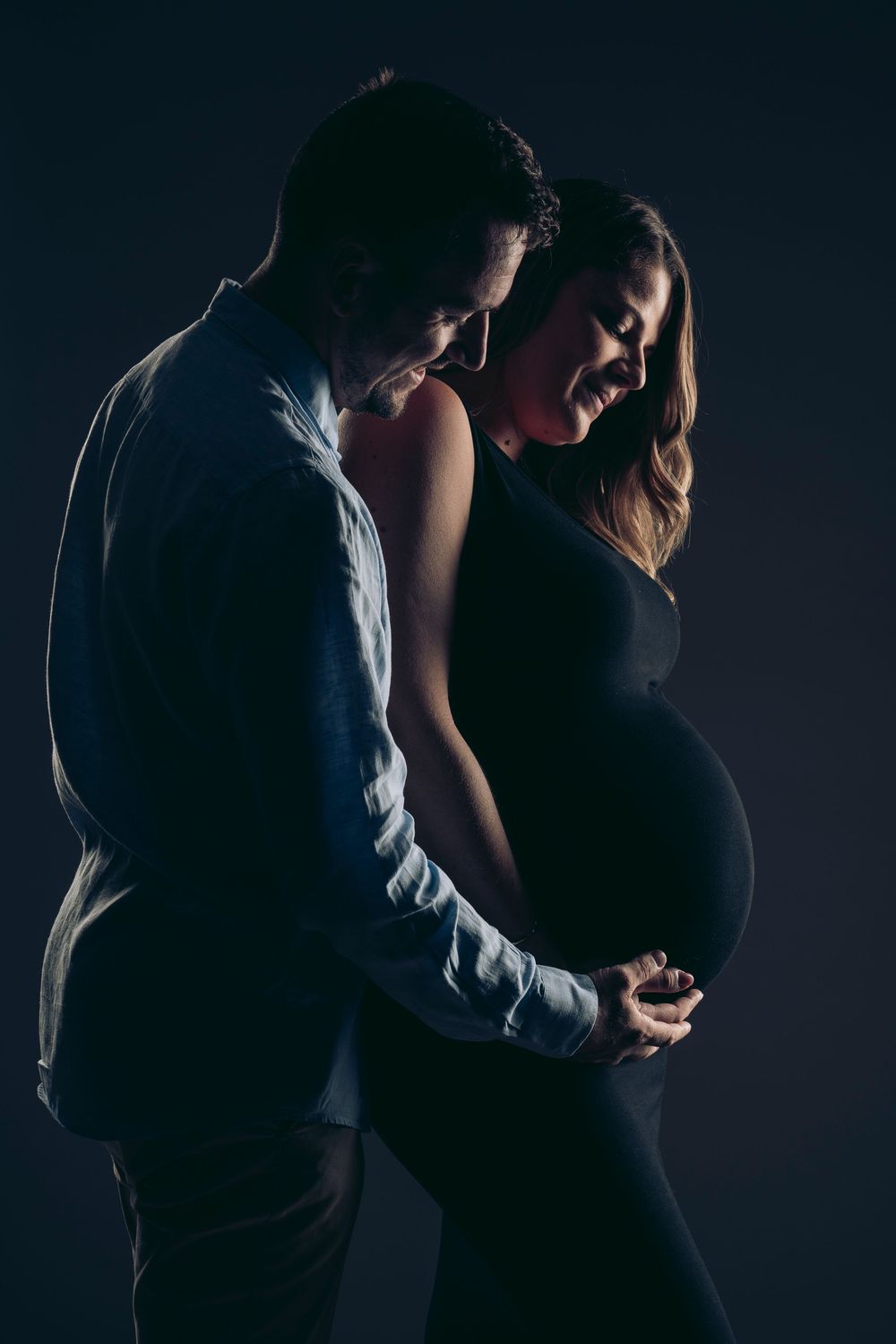 A silhouetted couple embraces intimately in a series of dark, moody photographs against a black background.