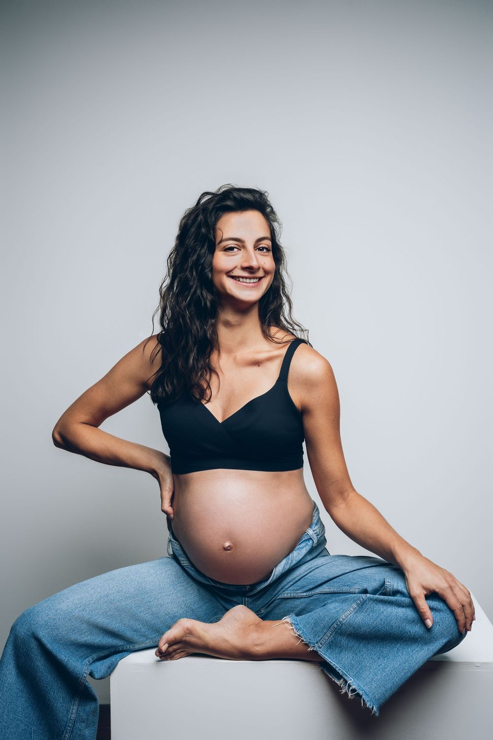 Artistic maternity photography series showing a pregnant woman in denim against a gray backdrop.