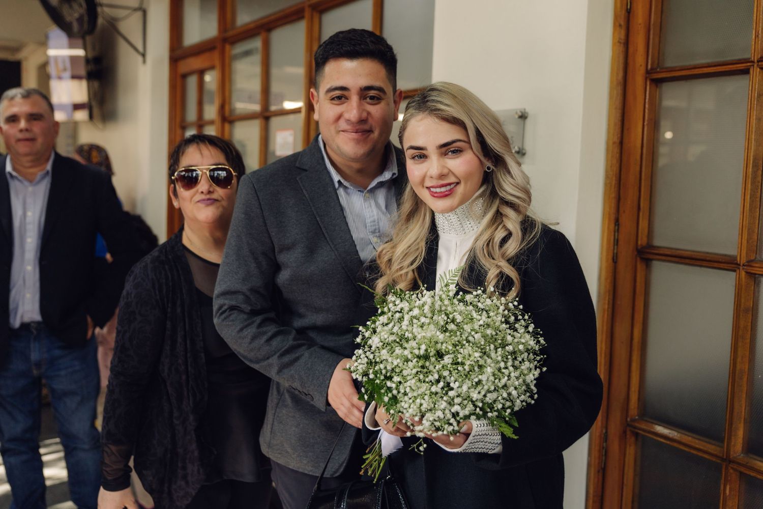 Smiling couple posing together at civil wedding ceremony, bride holding baby's breath bouquet indoors.