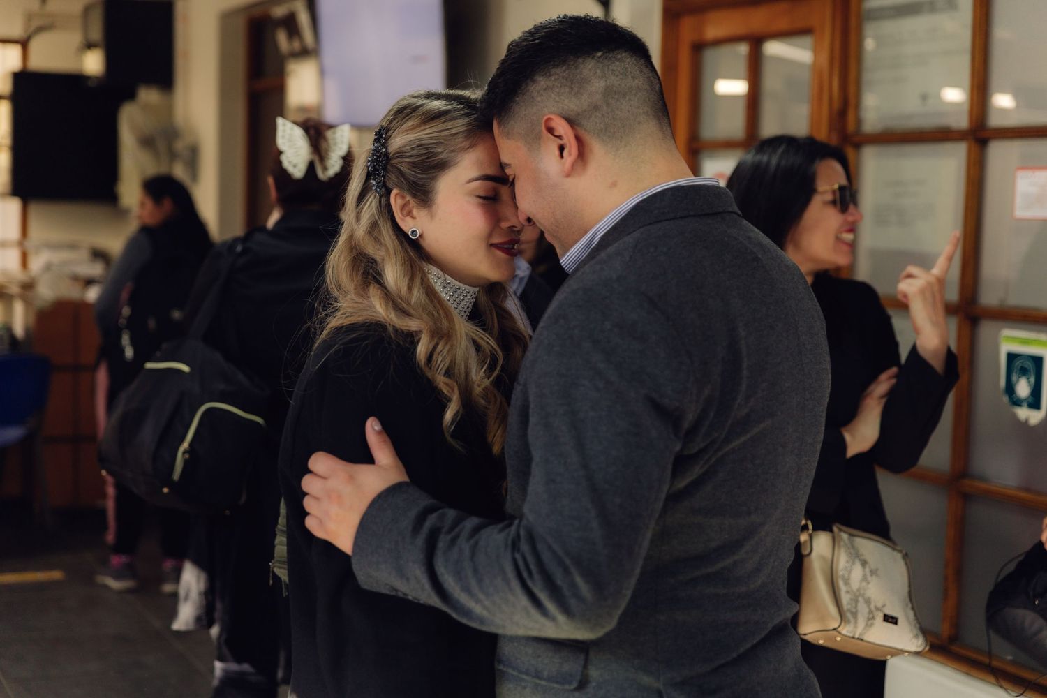 Romantic couple embracing closely at an indoor venue with guests in background.