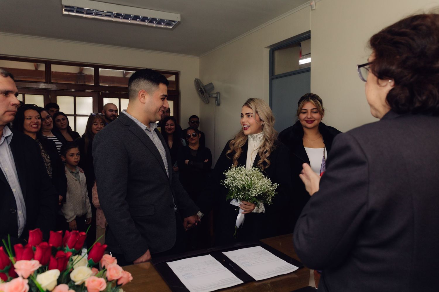 Bride holding baby's breath bouquet stands with groom before officiant during intimate civil wedding ceremony.