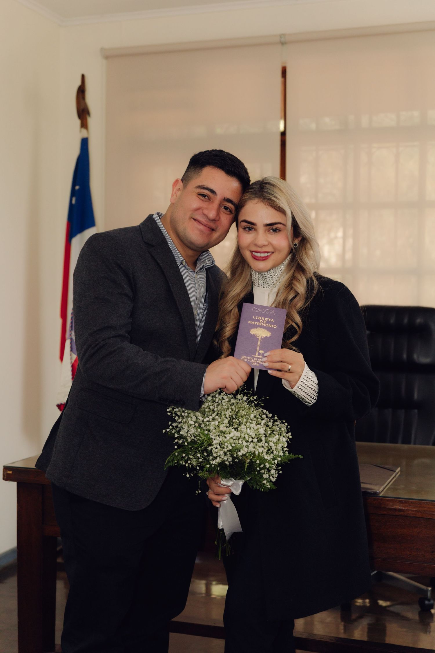 Couple holds flowers and a document, smiling at a civil wedding ceremony.