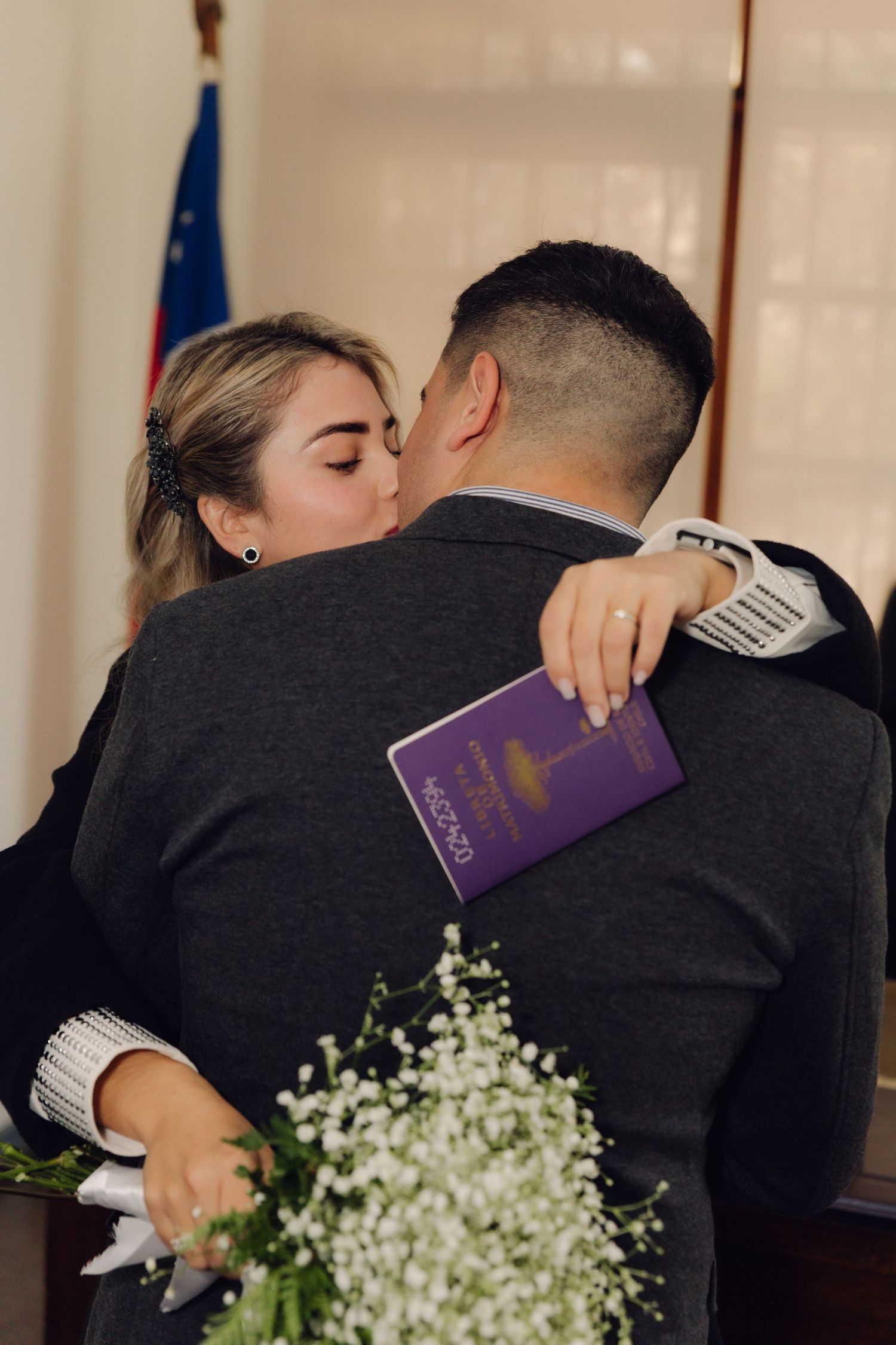 Couple shares a kiss after civil wedding ceremony, holding marriage document.