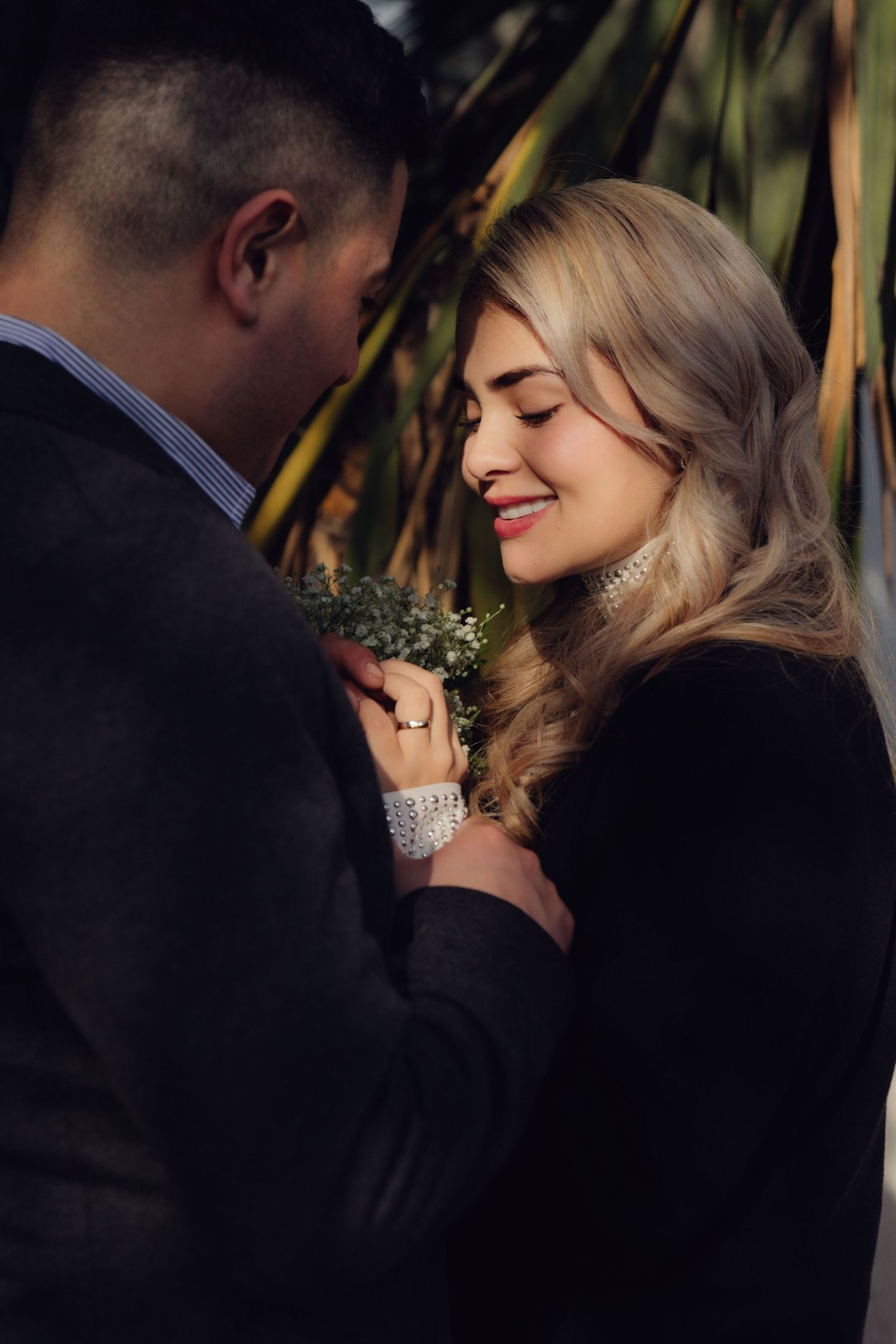 Smiling blonde bride with eyes closed holds flowers close to groom.