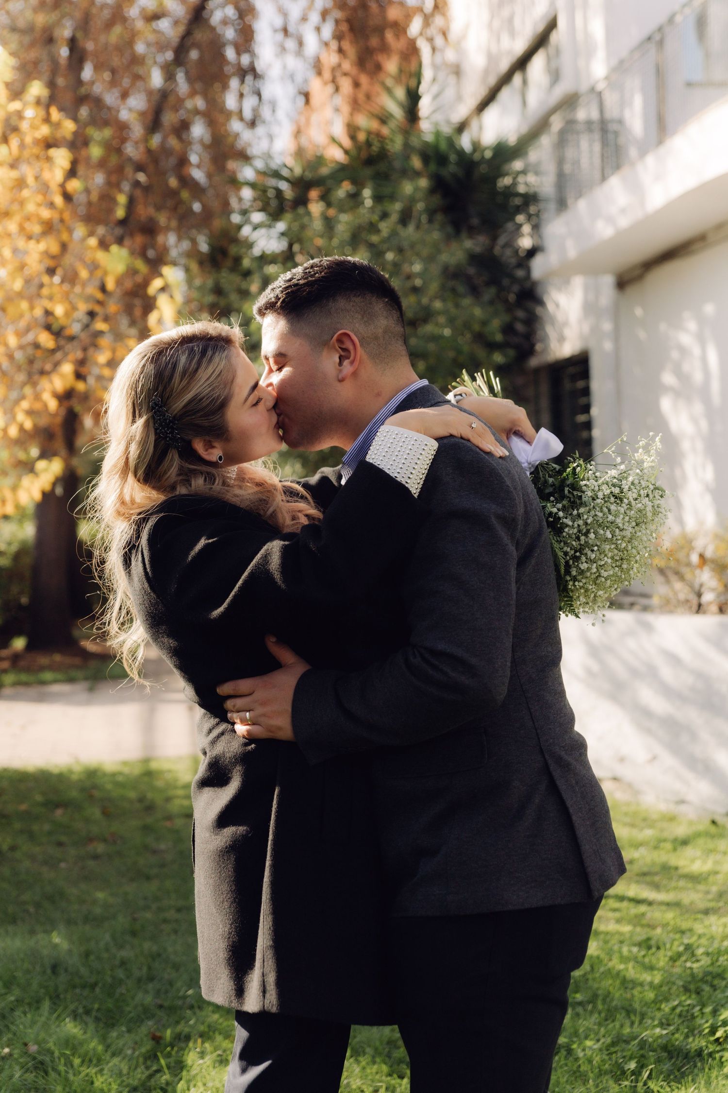 Newlywed couple shares a passionate kiss in a sunny outdoor garden.