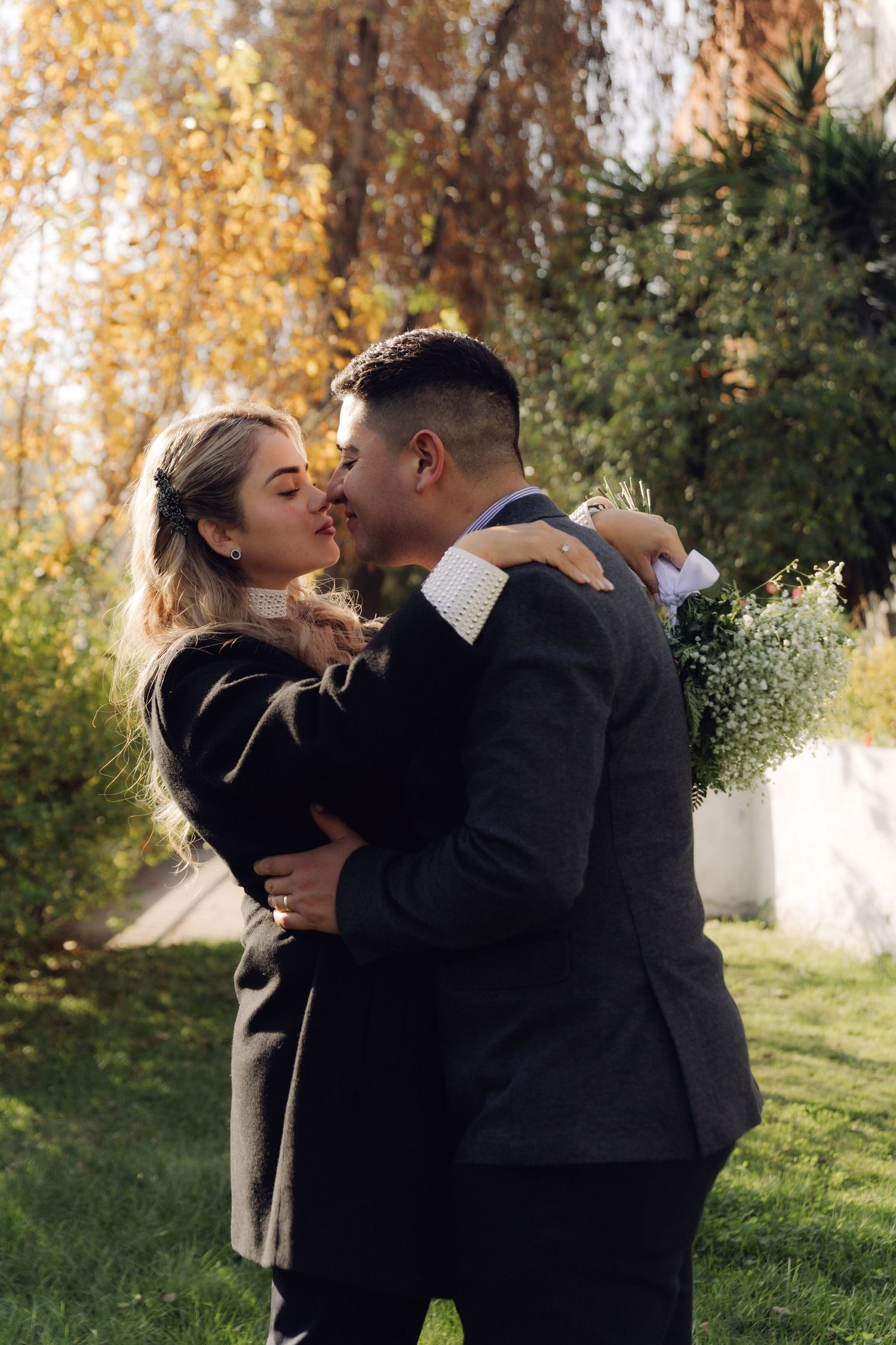 Couple kisses romantically outdoors surrounded by golden autumn foliage and greenery.