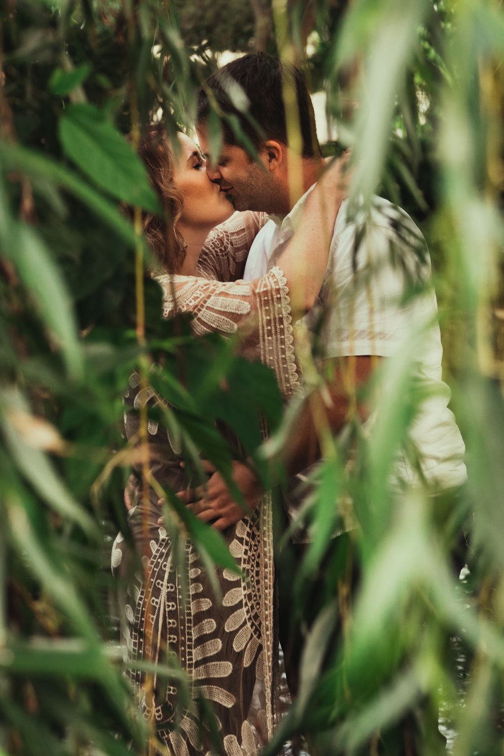 Portrait of a couple kissing behind tree vines hanging down.