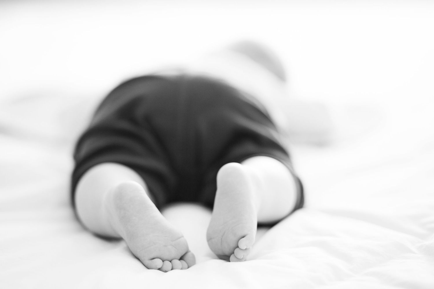 A black and white close-up photograph shows tiny baby toes against soft white fabric.