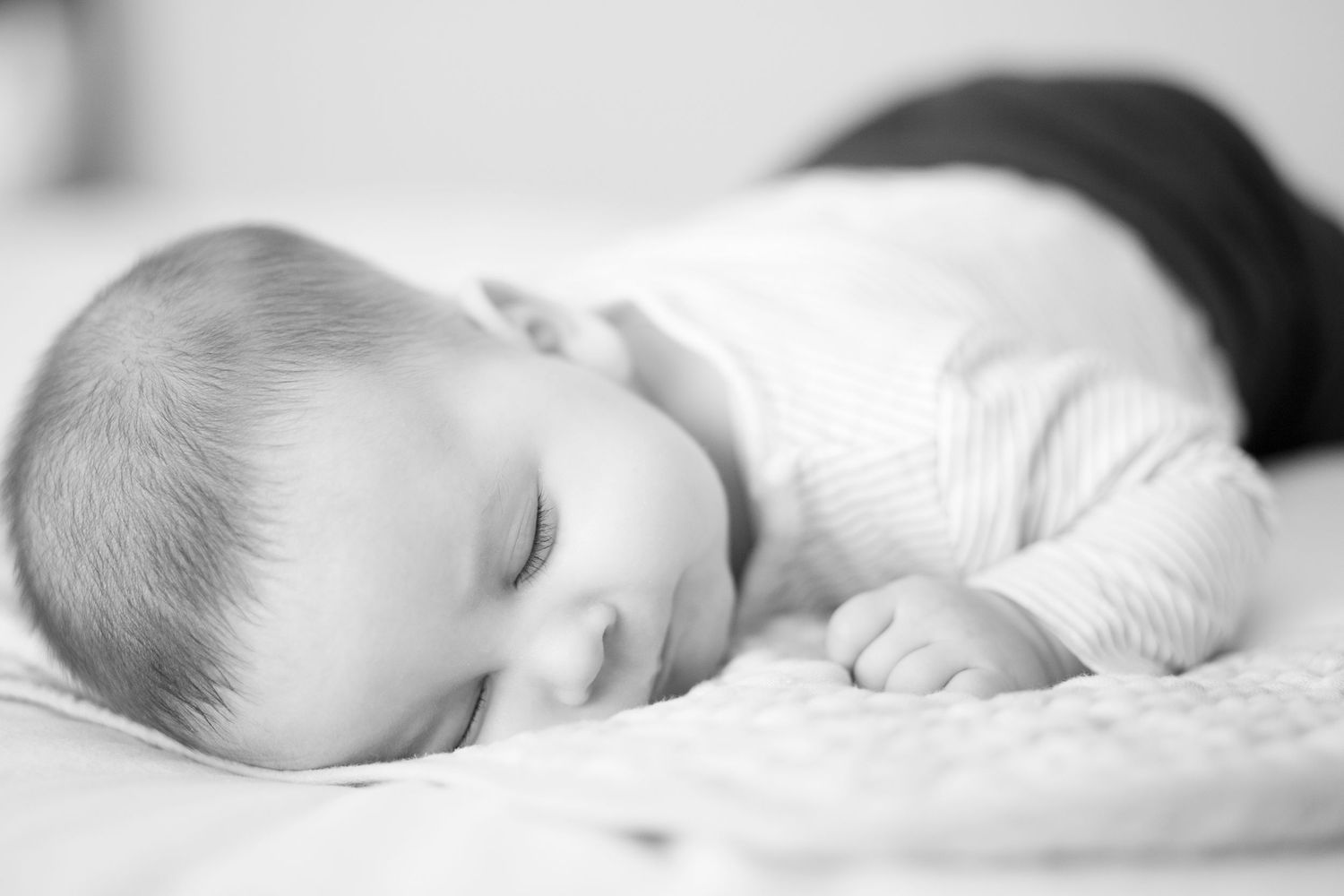 A sleeping baby rests peacefully on white bedding in a series of black and white photographs.