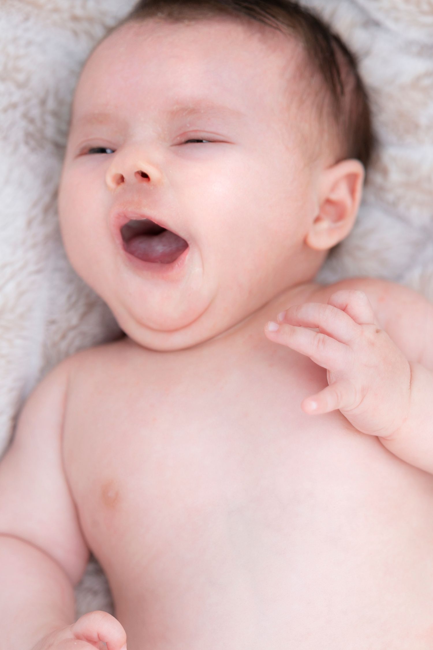 Baby resting on plush white blanket making expressive faces.
