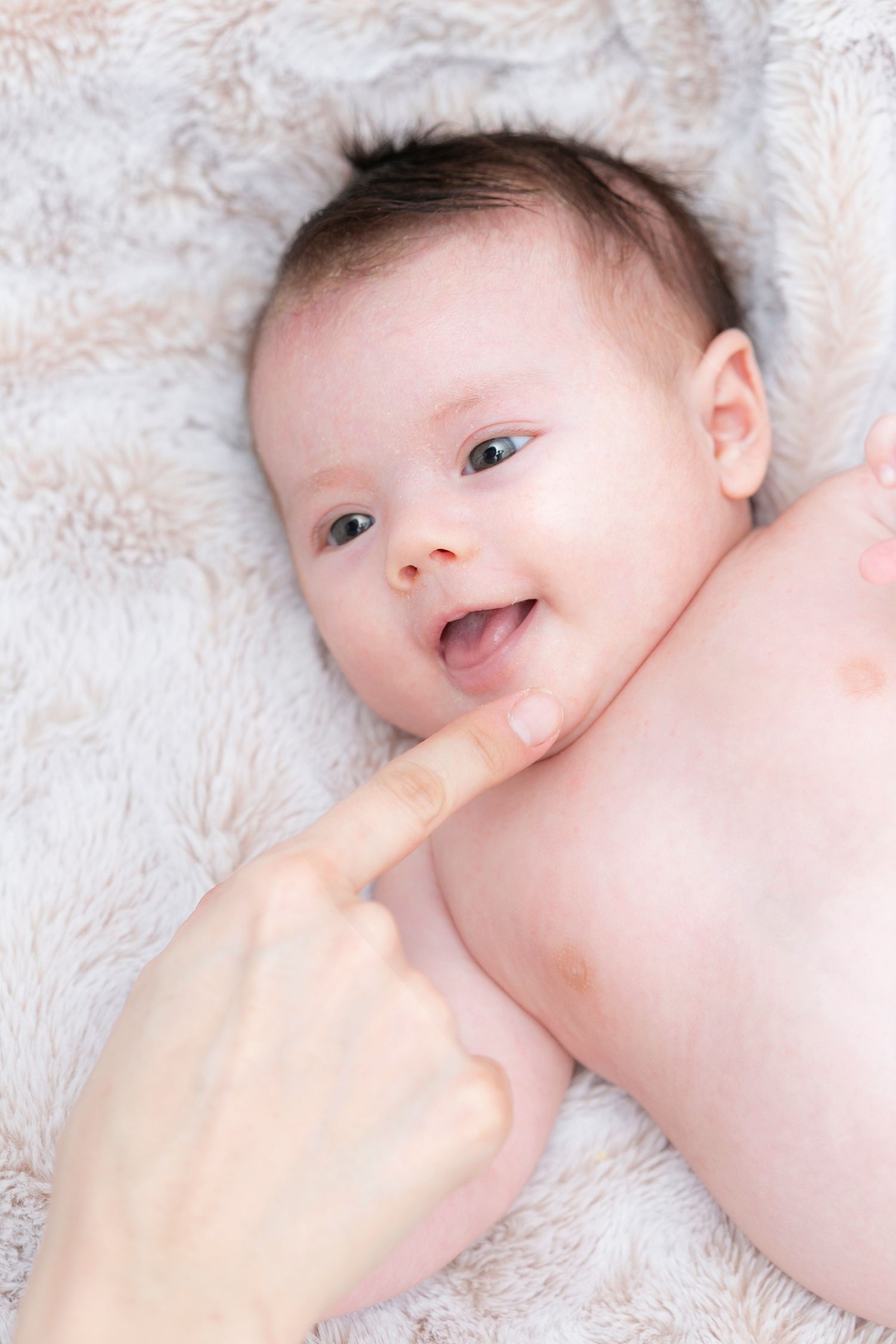 Baby lying on fluffy white blanket with gentle hand touching their cheek.