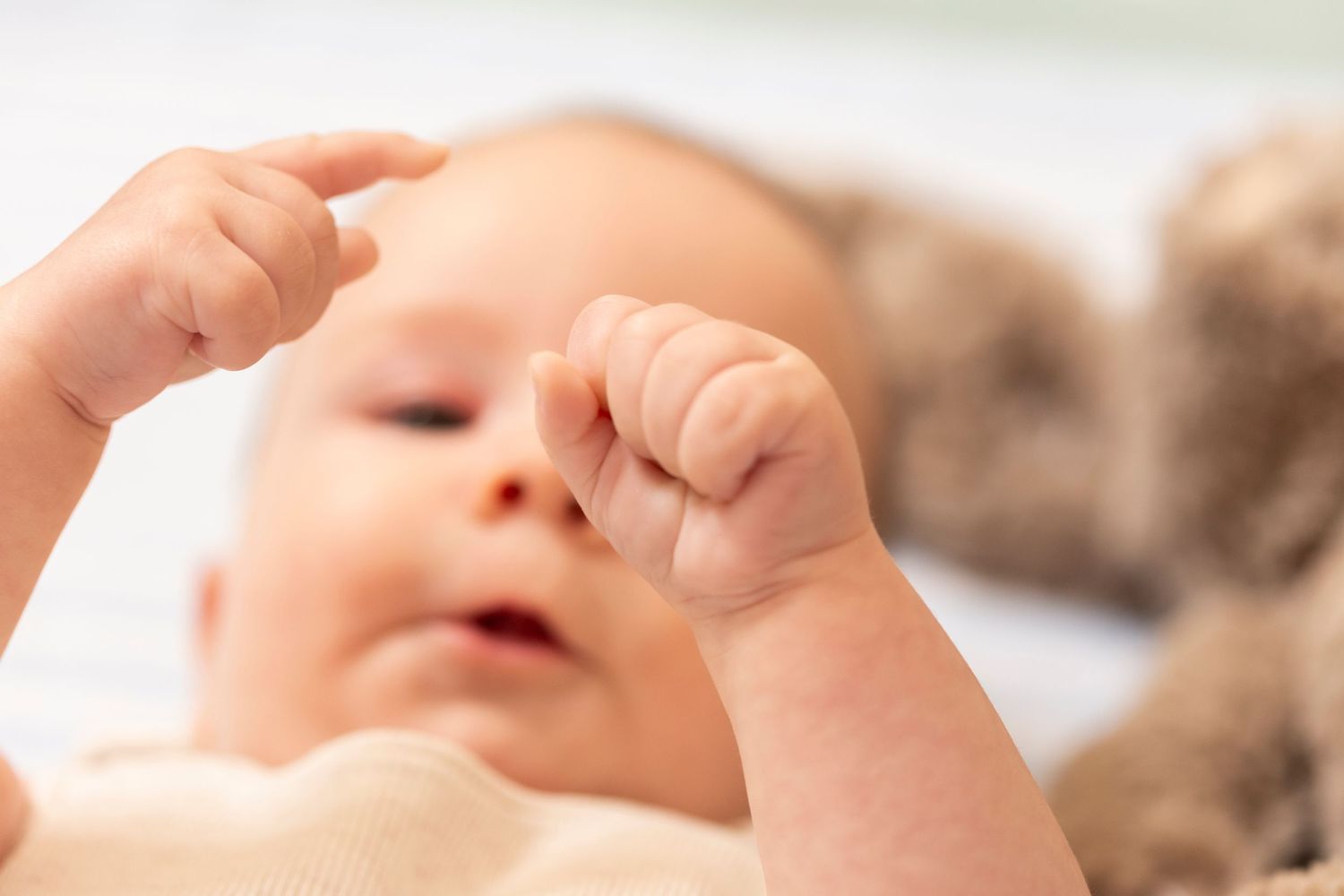Close-up view of a newborn baby's tiny hands reaching upward against a soft white background.