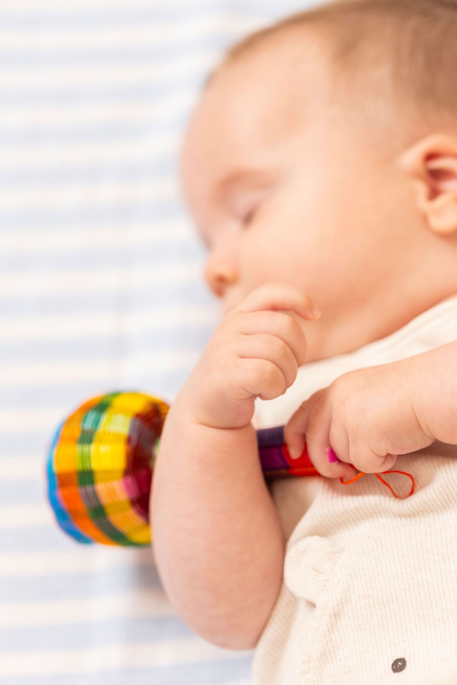 Close-up of baby in cream colored clothing with a rainbow-colored toy nearby.