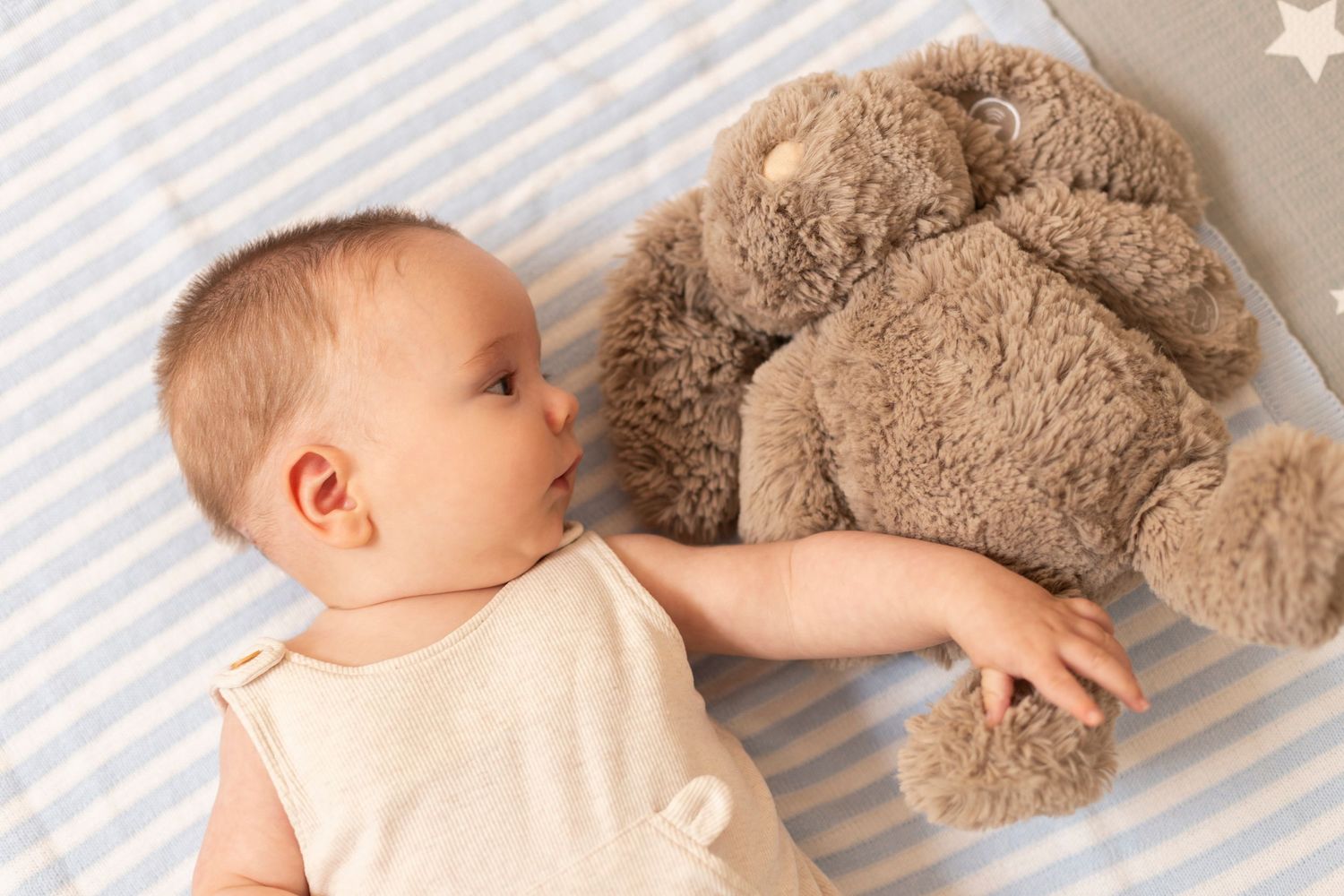 A sleeping baby lies on white bedding next to a large plush teddy bear.