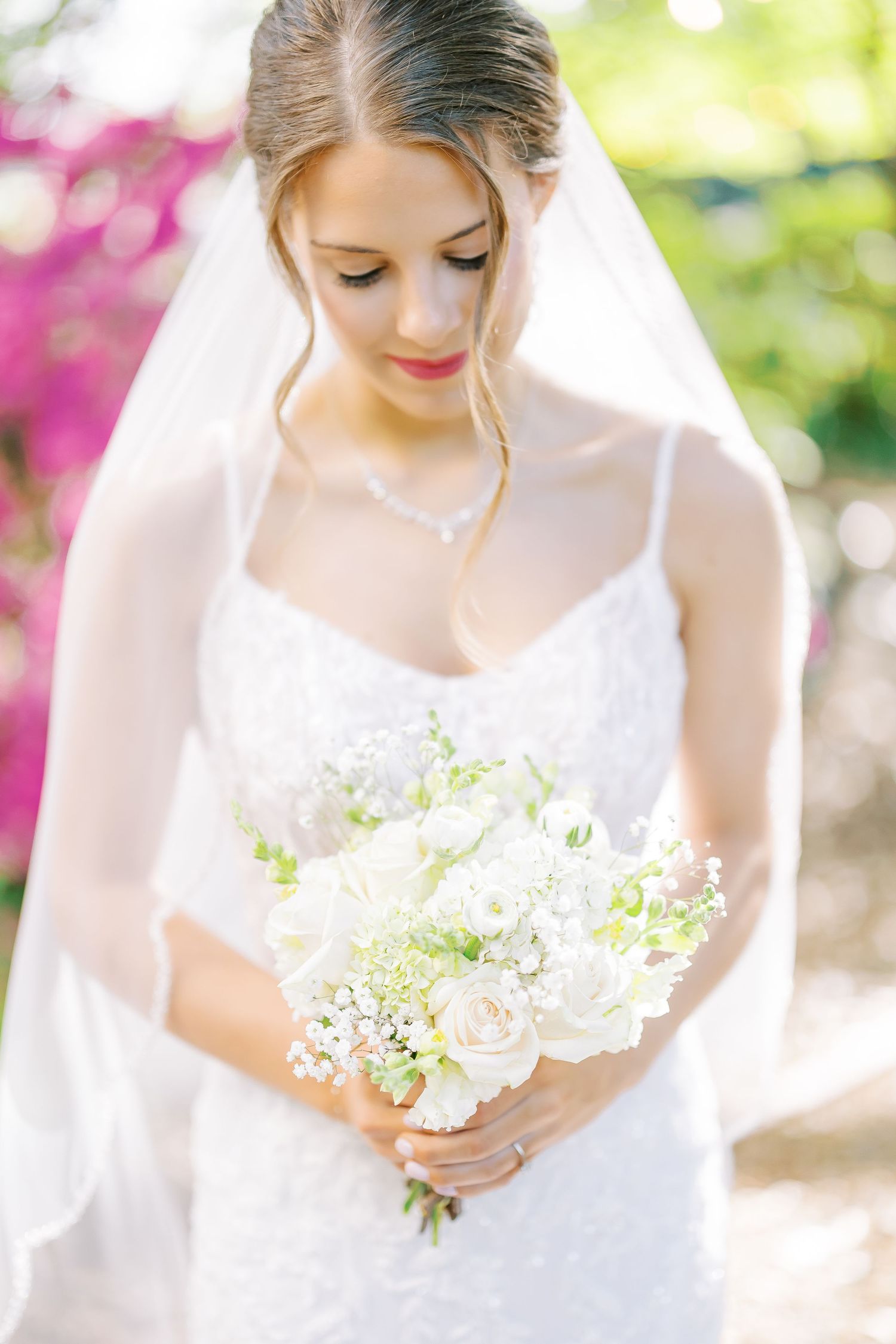 A person in a white dress holds a delicate bouquet of white flowers in a garden setting with pink blooms in background.