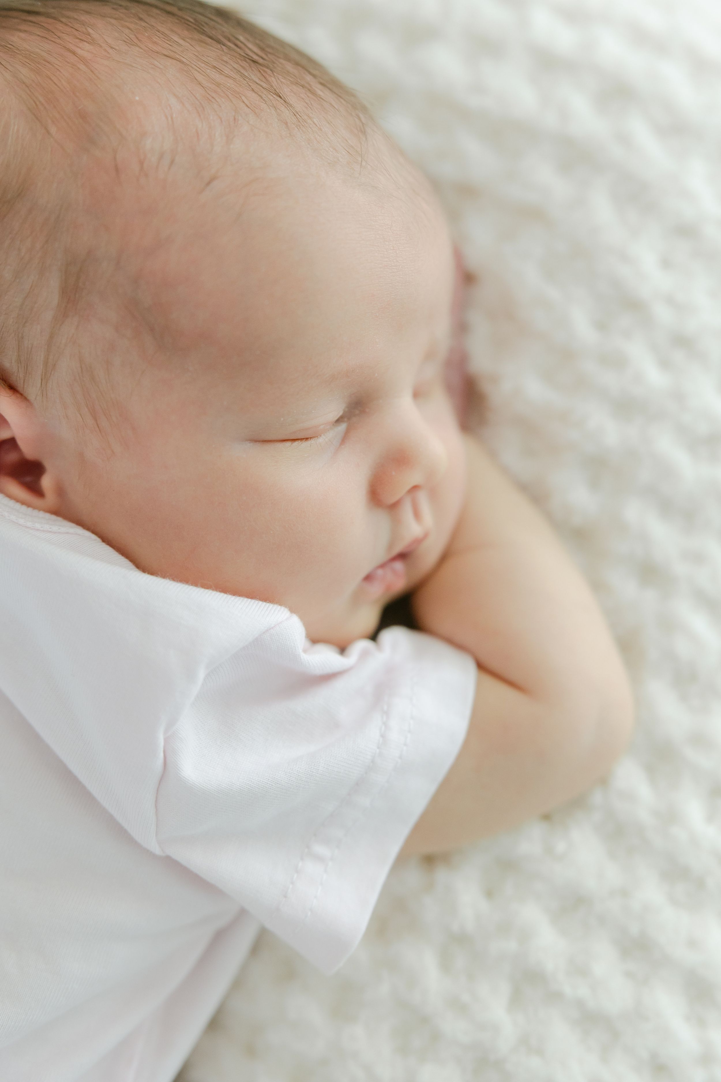 A sleeping baby in white clothing rests peacefully on soft white textured fabric. Hartford Newborn Photography Studio.