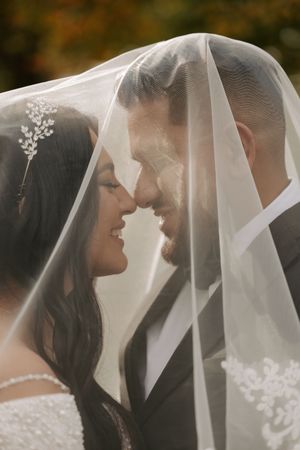 Romantic wedding couple shares an intimate moment under a delicate white veil during their outdoor ceremony.