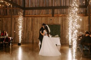Couple dancing in a rustic barn venue illuminated by sparklers and string lights during their wedding celebration.