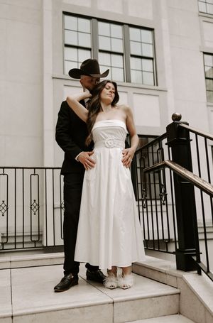 Couple embraces on white stone steps with iron railings in formal wear.