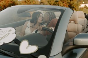 Newlyweds sharing a romantic moment in a convertible decorated with heart ornaments.