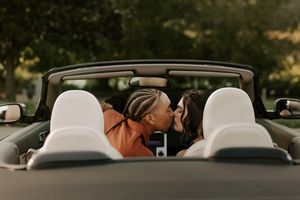Romantic couple kissing in a convertible car during sunset.