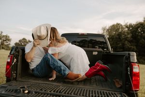 A couple relaxes together in the bed of a pickup truck at sunset.