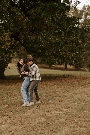 Couple jumping and playing together on a hillside during fall.