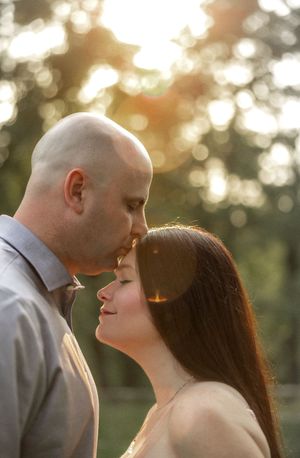 A romantic couple shares an intimate moment at sunset in a park with beautiful bokeh lighting effects.