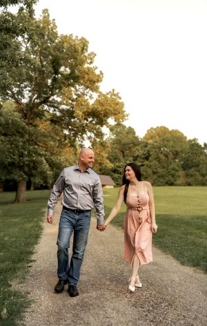 A couple takes a romantic stroll together on a gravel path through a scenic park at golden hour.