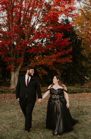 Couple poses beneath vibrant red maple trees during autumn wedding photoshoot.
