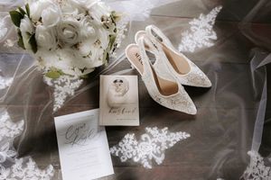 Wedding details flatlay with white shoes, invitation and floral bouquet on lace.