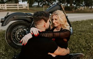 An intimate moment between a couple cuddling next to a motorcycle outdoors.