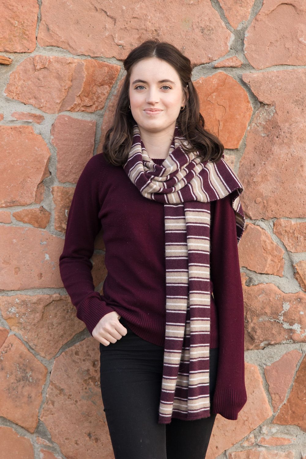 A cozy burgundy sweater paired with a striped scarf against a rustic stone wall.
