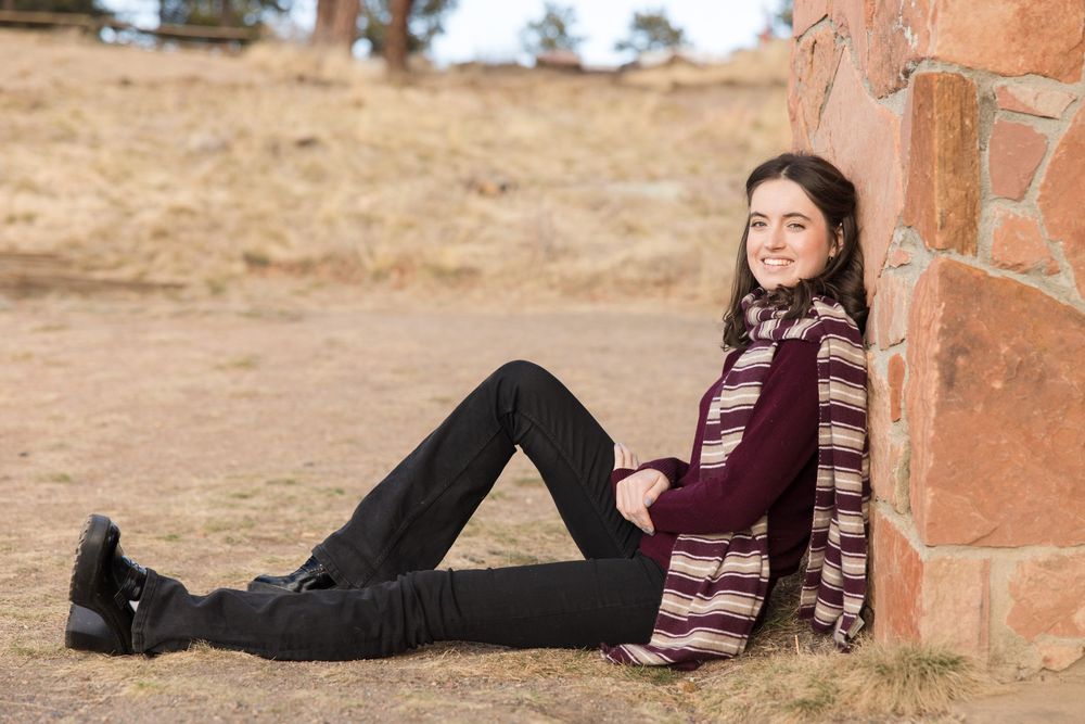 Person in casual attire relaxing against a brick wall outdoors.