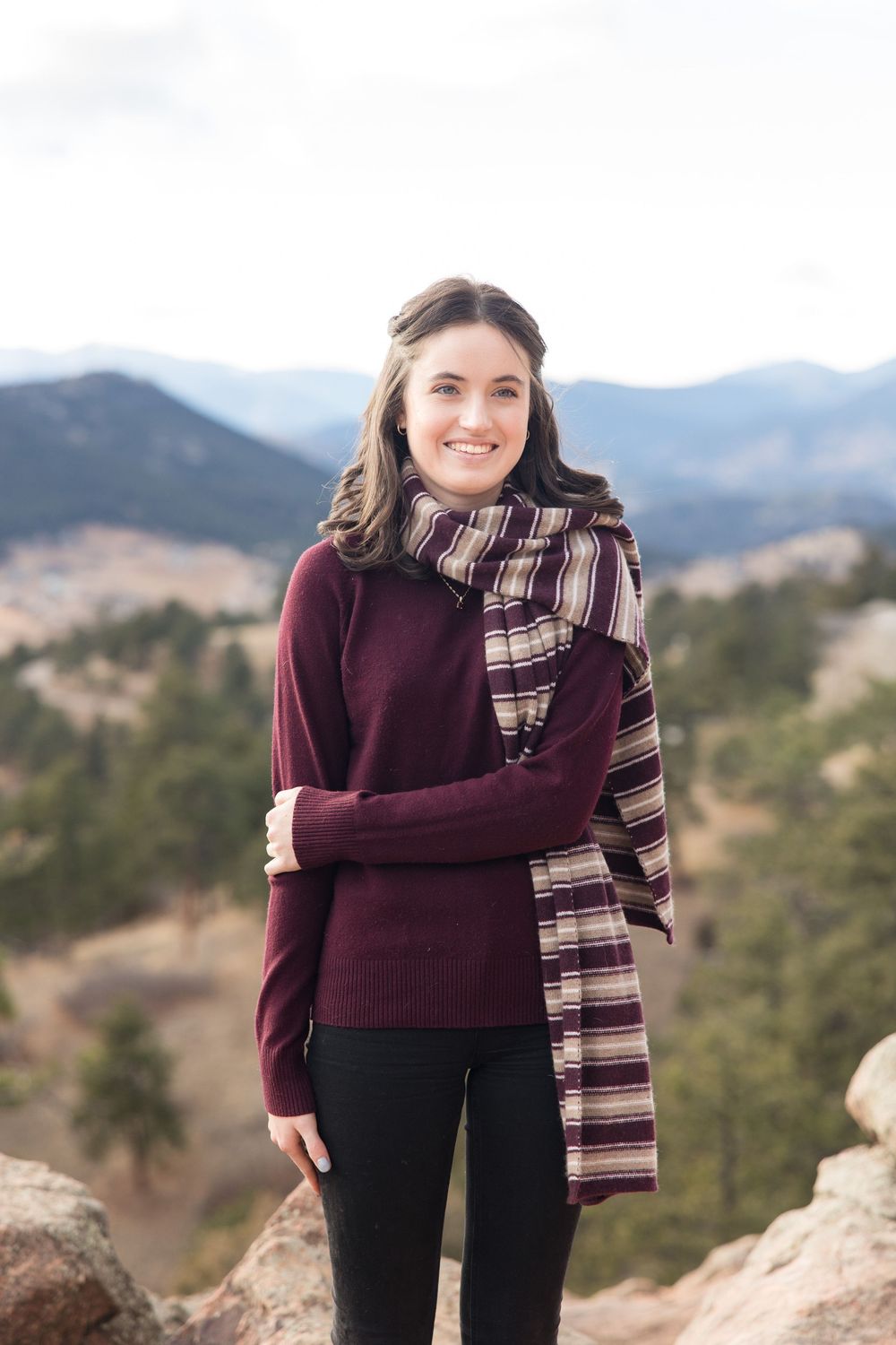 A burgundy sweater and striped scarf outfit worn against a scenic mountain backdrop.