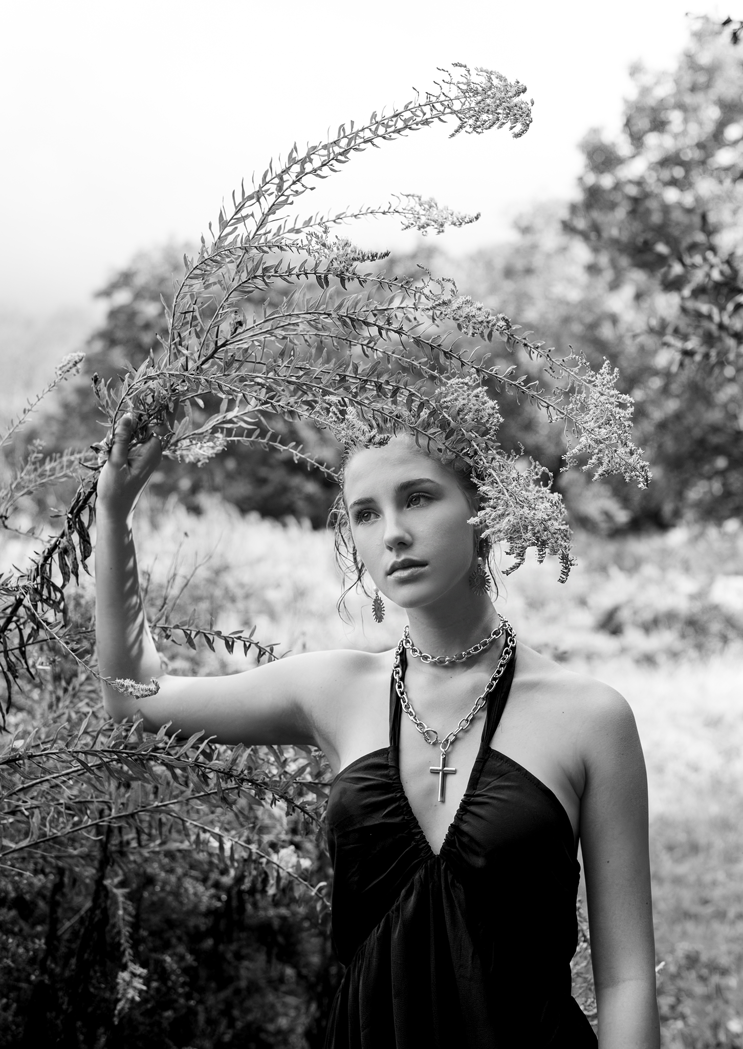 Black and white portrait of young woman in black halter dress holding wild plant branches outdoors.