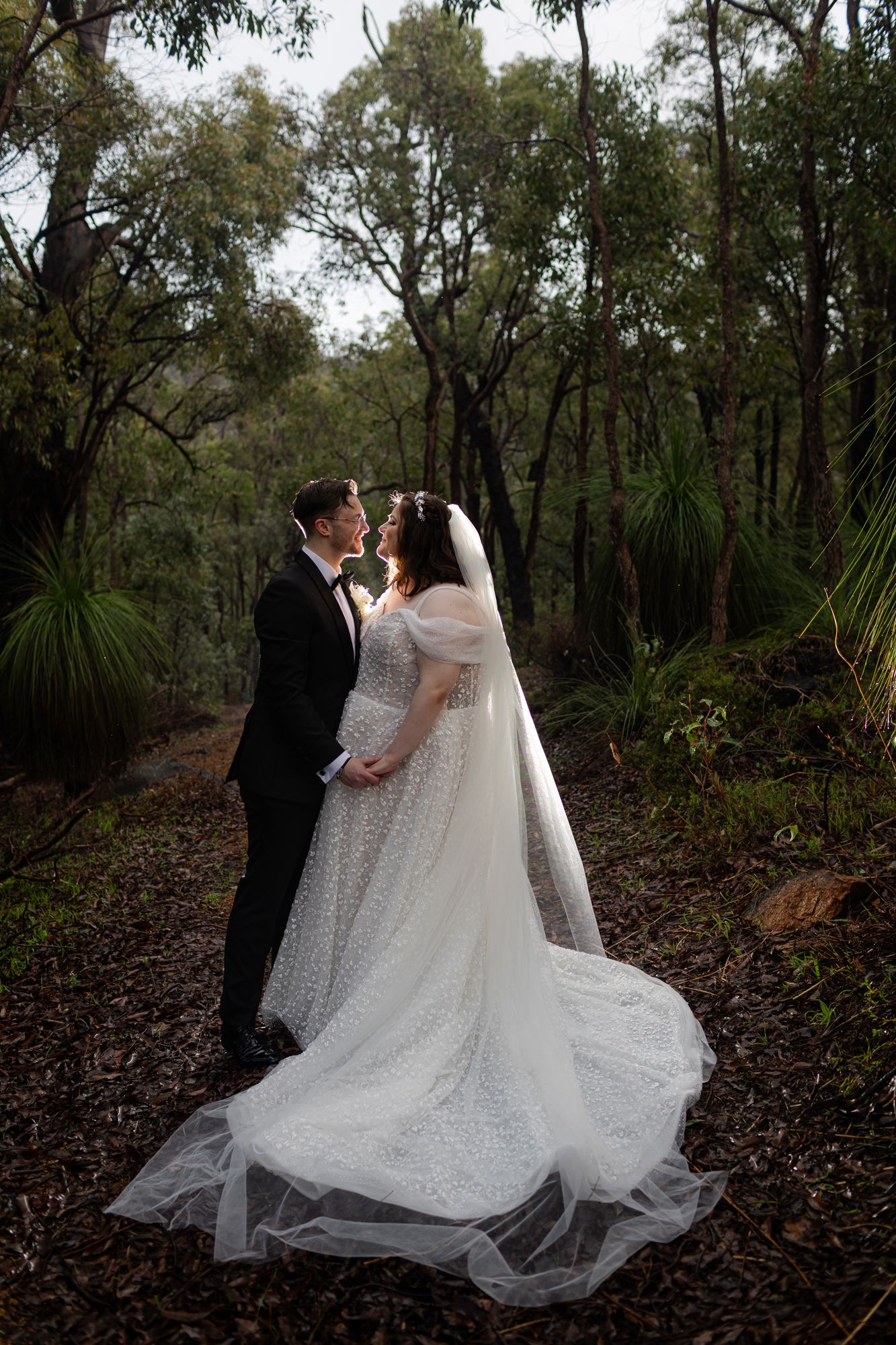 A wedding couple poses outside a gothic stone church as the bride's veil dramatically catches the wind.