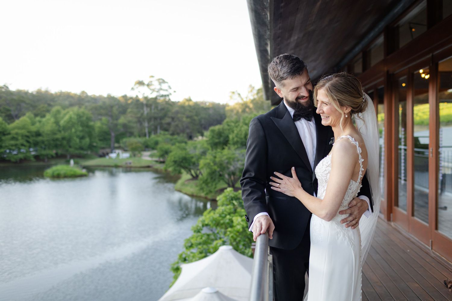 A couple in wedding attire walks together along a brick building exterior while sharing a joyful moment.