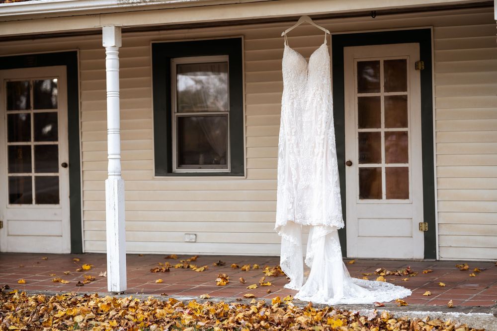 White farmhouse porch decorated with autumn pumpkins and fall leaves scattered on the ground.