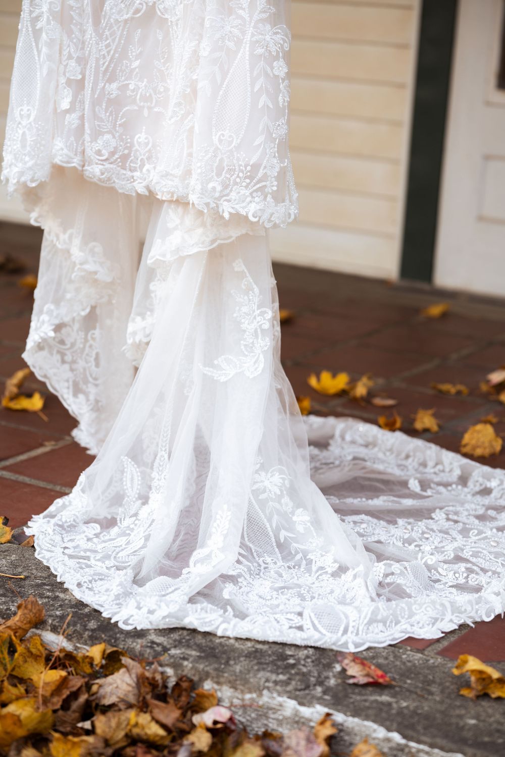 Elegant white lace wedding dress train trailing over brick steps with scattered autumn leaves.