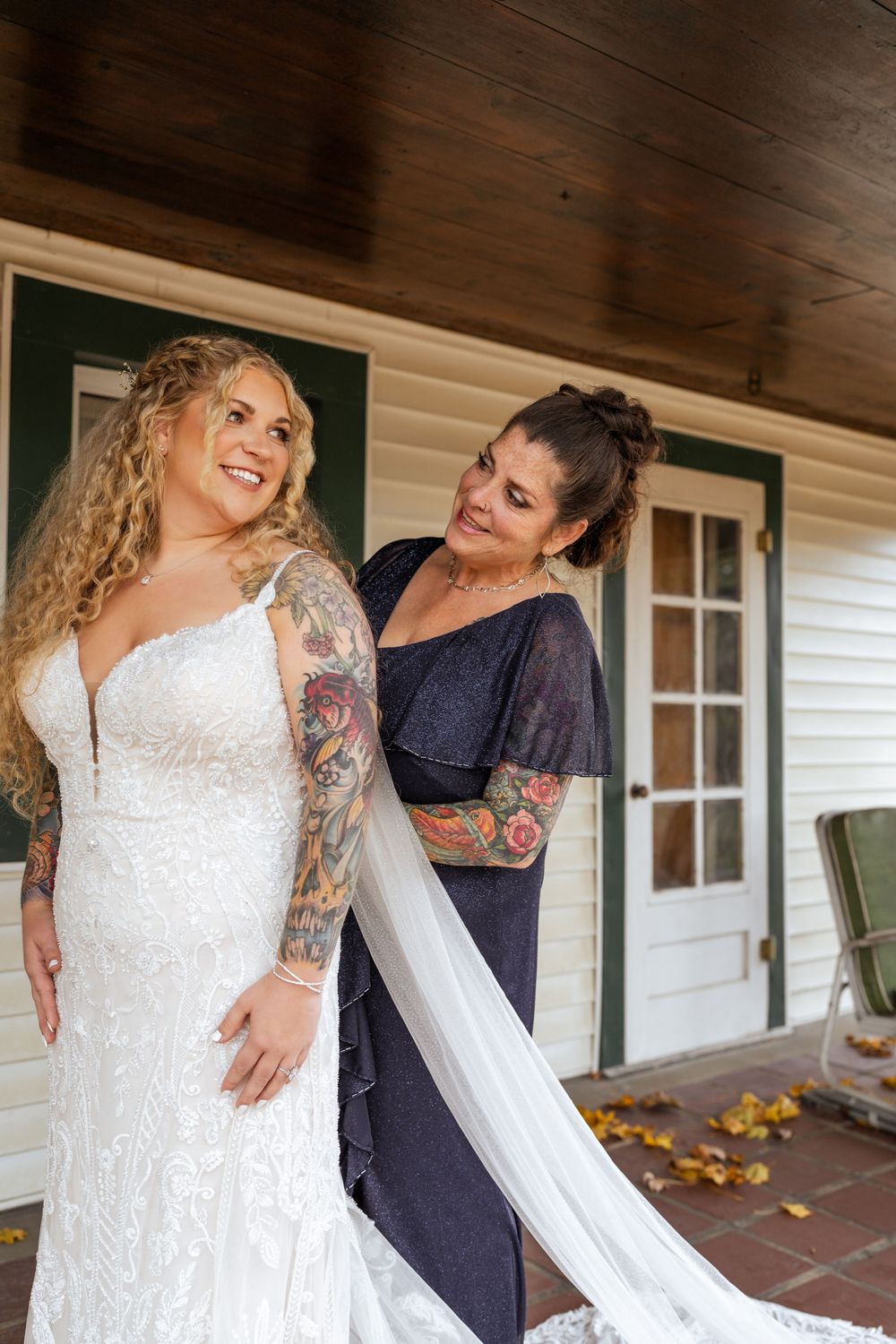 Bride in white lace wedding dress with flowing veil getting ready on porch of white house.