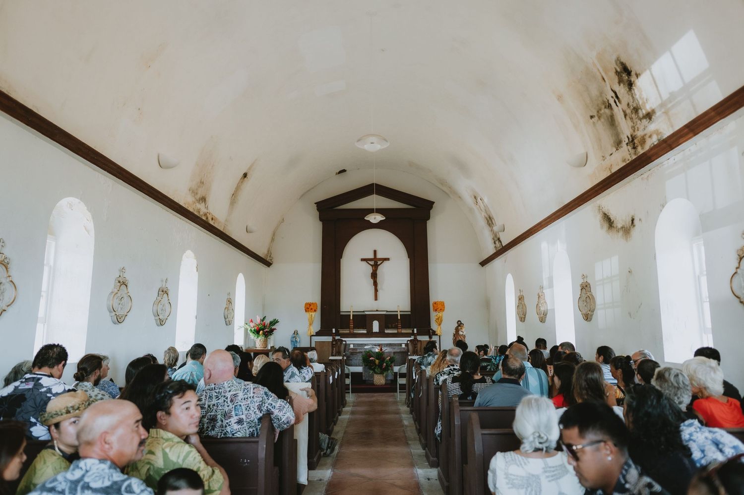 Interior of a traditional white church filled with wedding guests during a ceremony.