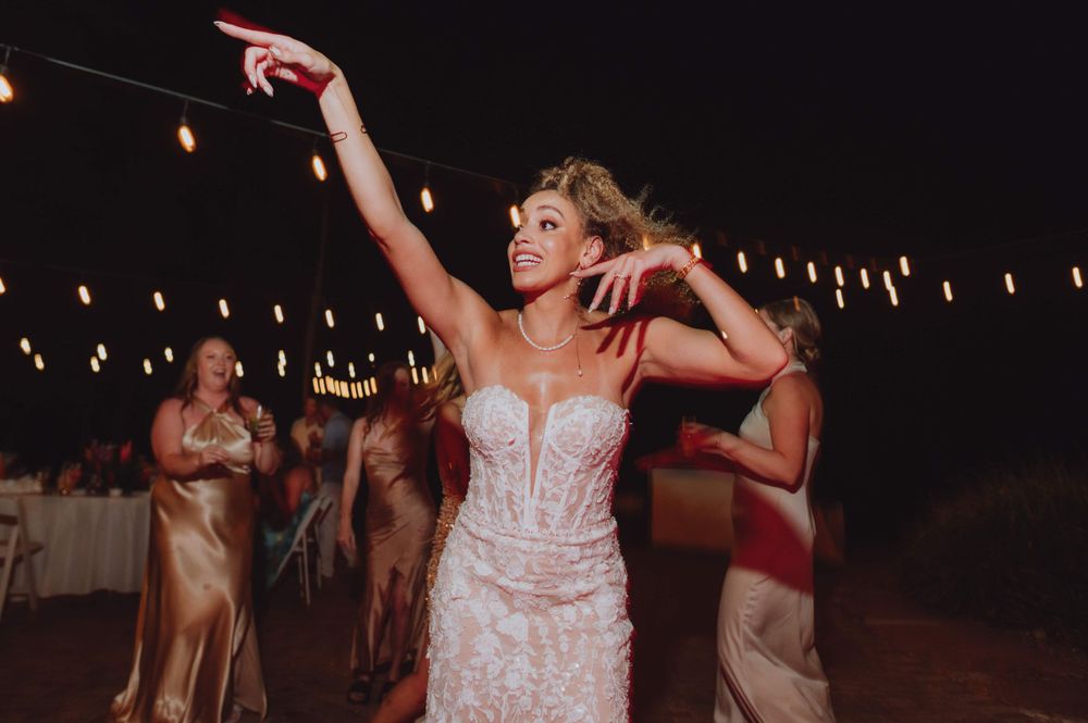 Wedding guests dance and point upward during an evening celebration.