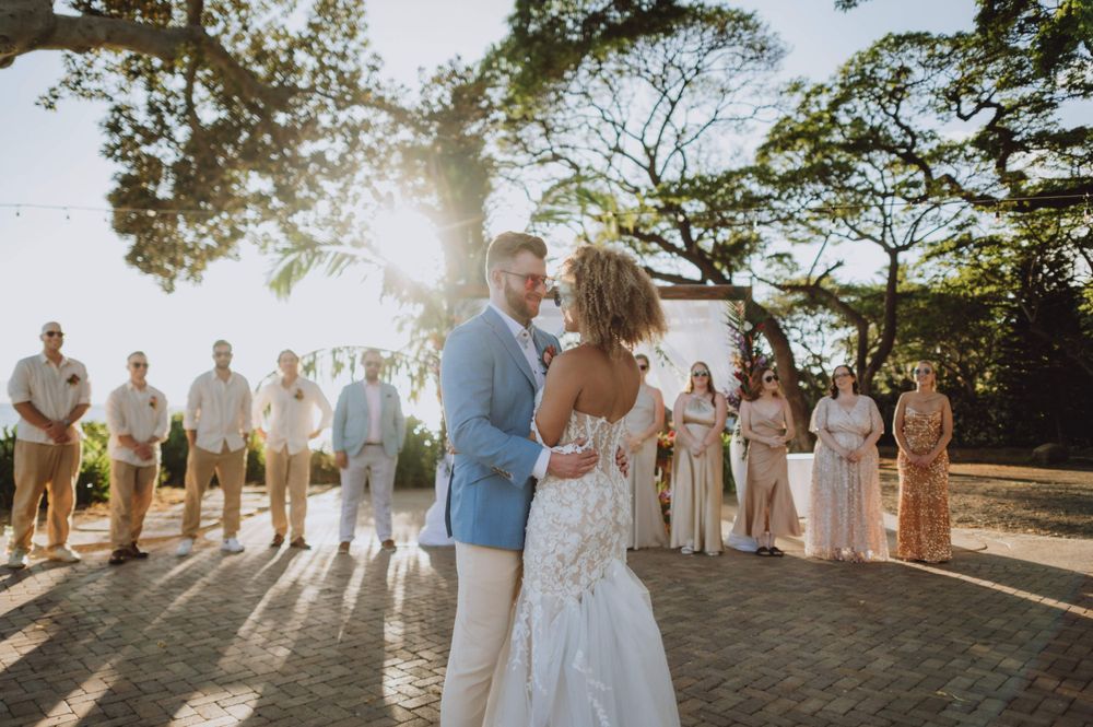Wedding party lined up during golden hour with sun flare and trees in the background.