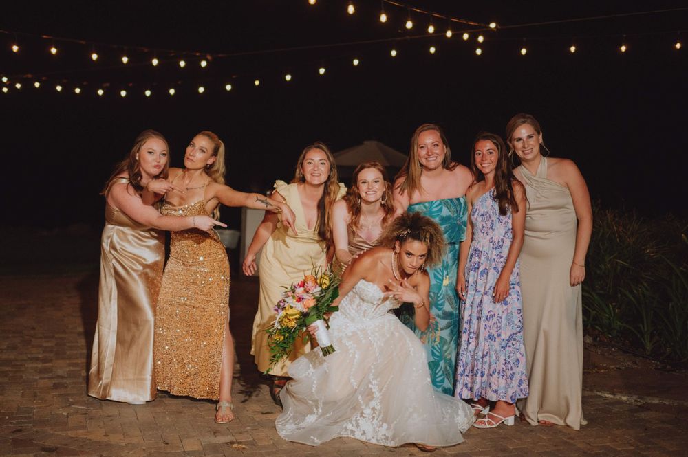 Wedding party poses together under twinkling string lights at an outdoor evening celebration.