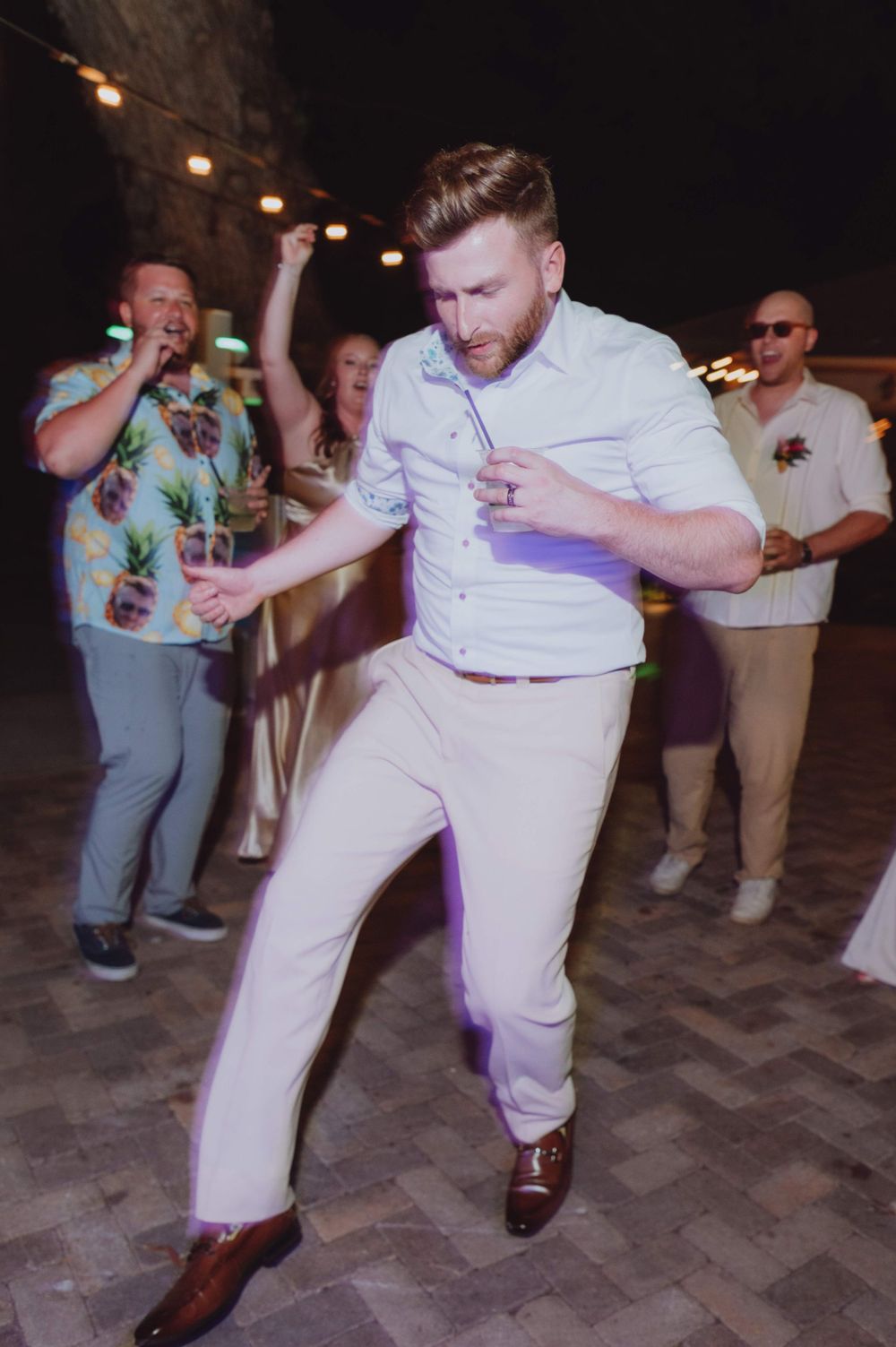 Groomsmen perform synchronized dance moves in white shirts and khaki pants at a wedding.