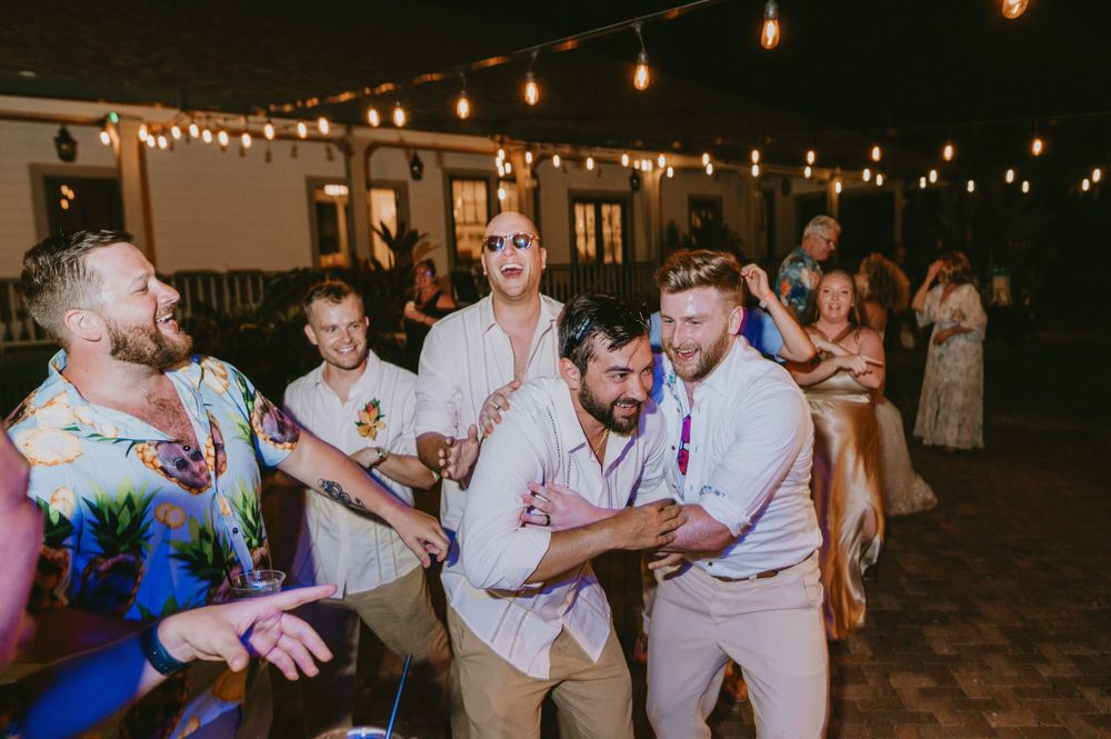 Wedding guests dance and celebrate under string lights at an outdoor reception.