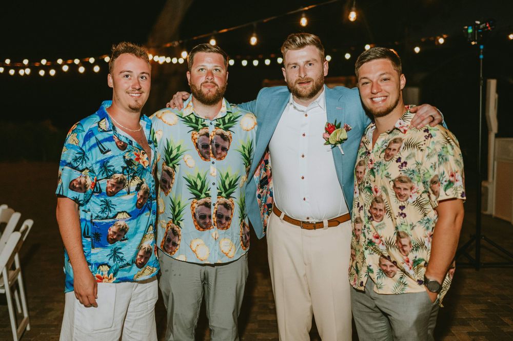 Wedding party members wearing tropical floral shirts and gray pants pose together outdoors.
